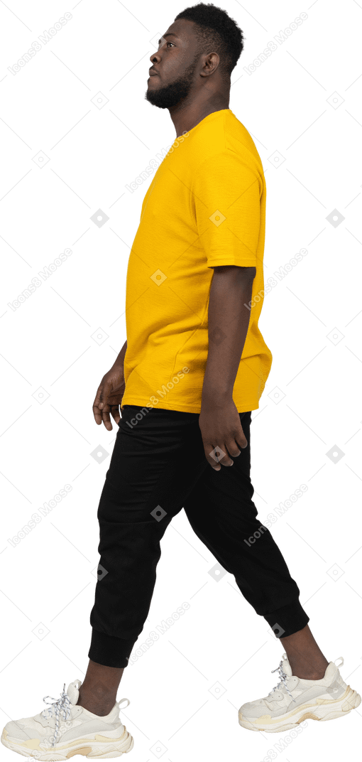 一个穿着黄色 t 恤的黑皮肤青年行走的侧视图