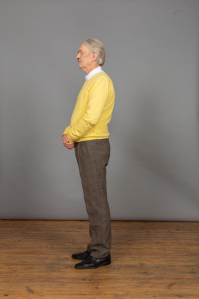 Side view of an old man in yellow pullover holding hands together with his eyes closed