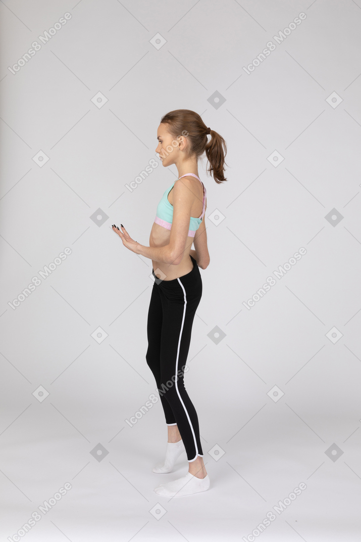 Vista lateral de una jovencita en ropa deportiva bailando mientras gesticula