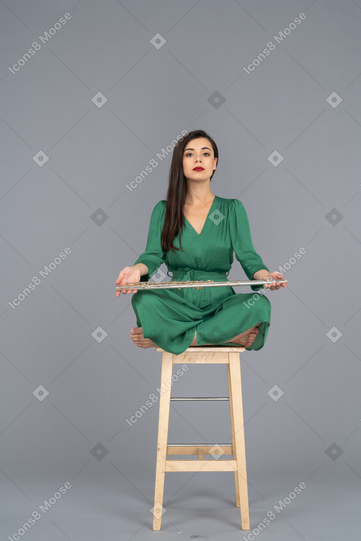 Full-length of a young lady holding her clarinet on her knees while sitting on a wooden chair