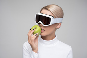 Woman in ski goggles about to bite from a green apple
