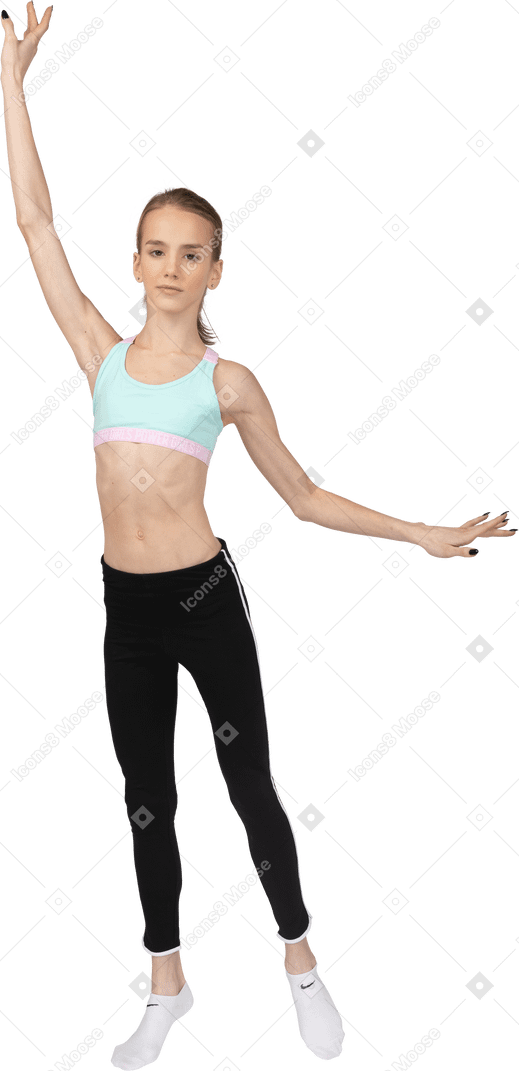 Vista frontal de uma adolescente em roupas esportivas levantando as mãos e colocando a perna de lado