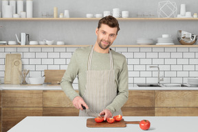 A man in a kitchen cutting tomatoes on a cutting board