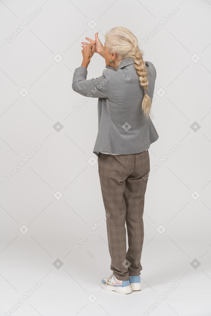 Rear view of an old lady in suit pointing with fingers