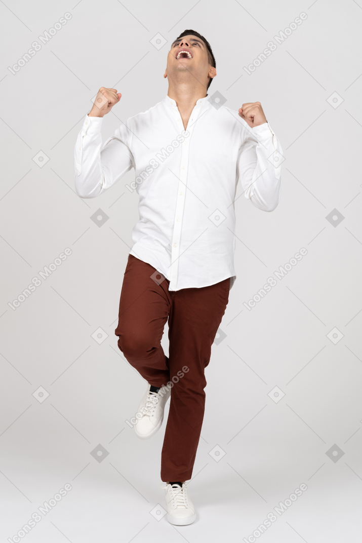 Front view of a young latino man jumping on one leg and clenching fists in excitement