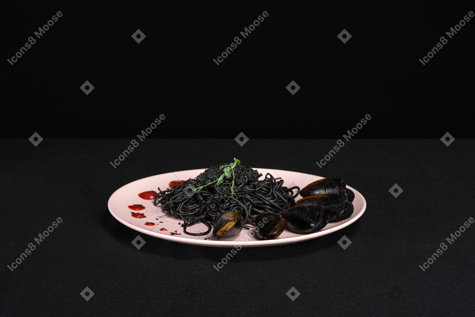 Black pasta with mussels on pink plate in black background