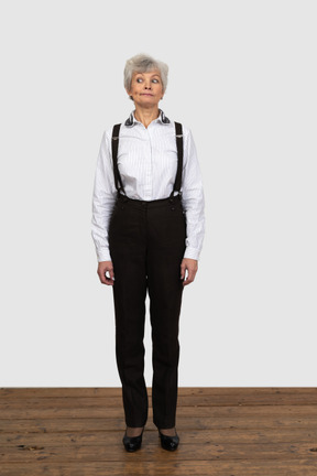 Vista frontal de una vieja mujer curiosa en ropa de oficina de pie todavía en el interior mirando a un lado