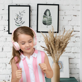 A little girl wearing headphones standing in front of a vase