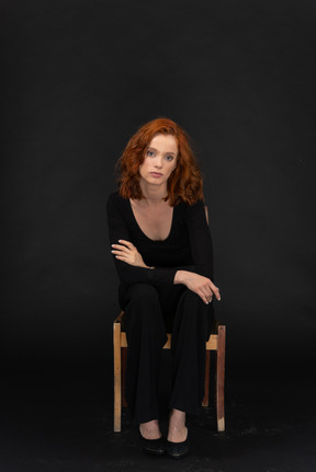 A frontal view of the cute young girl sitting on the wooden chair and looking to the camera