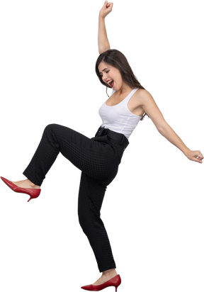 Вид сбоку счастливой молодой женщины в офисной одежде танцует и поднимает руку