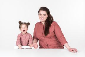 Mãe e sua filha, vestindo roupas vermelhas e rosa, se divertindo na mesa de jantar