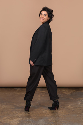 Back view of a happy businesswoman wearing black suit looking at camera and smiling