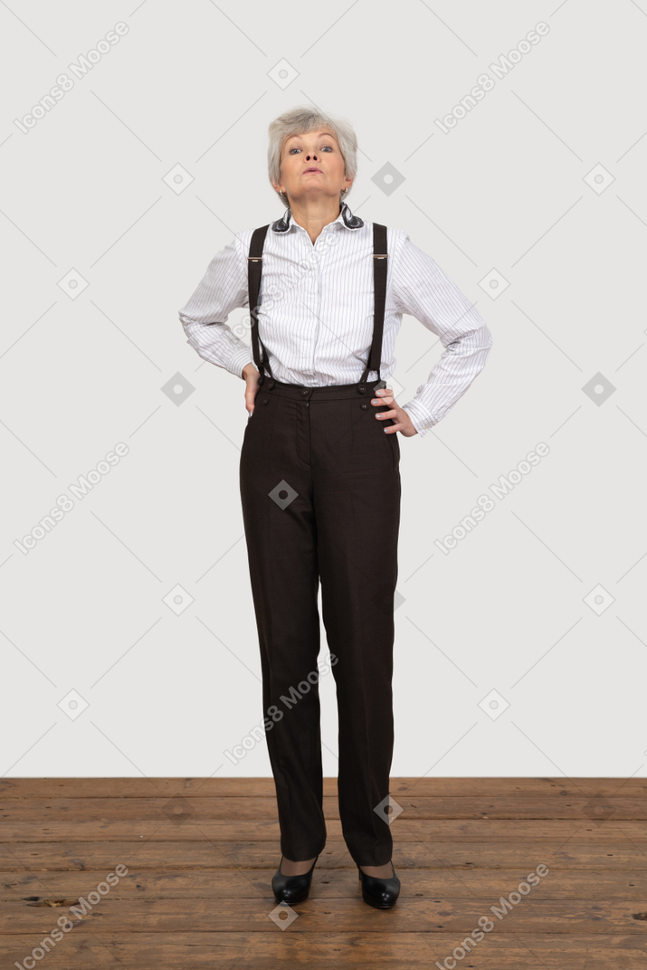 Vorderansicht einer unzufriedenen alten dame in bürokleidung, die hände auf hüften setzt