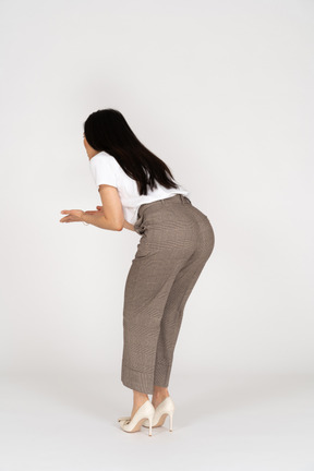 Three-quarter back view of a questioning  young lady in breeches and t-shirt raising hands and bending down