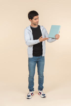 Young caucasian man pointing at book he's holding