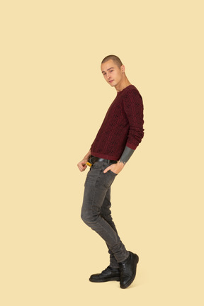 Side view of a young man in red pullover touching belt