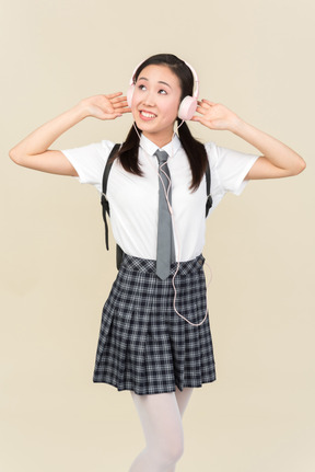 Asian school girl adjusting headphones and looking up