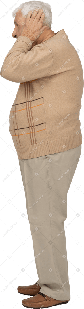 Vista lateral de un anciano con ropa informal que cubre las orejas con las manos