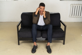 Front view of a perplexed young man sitting on a sofa