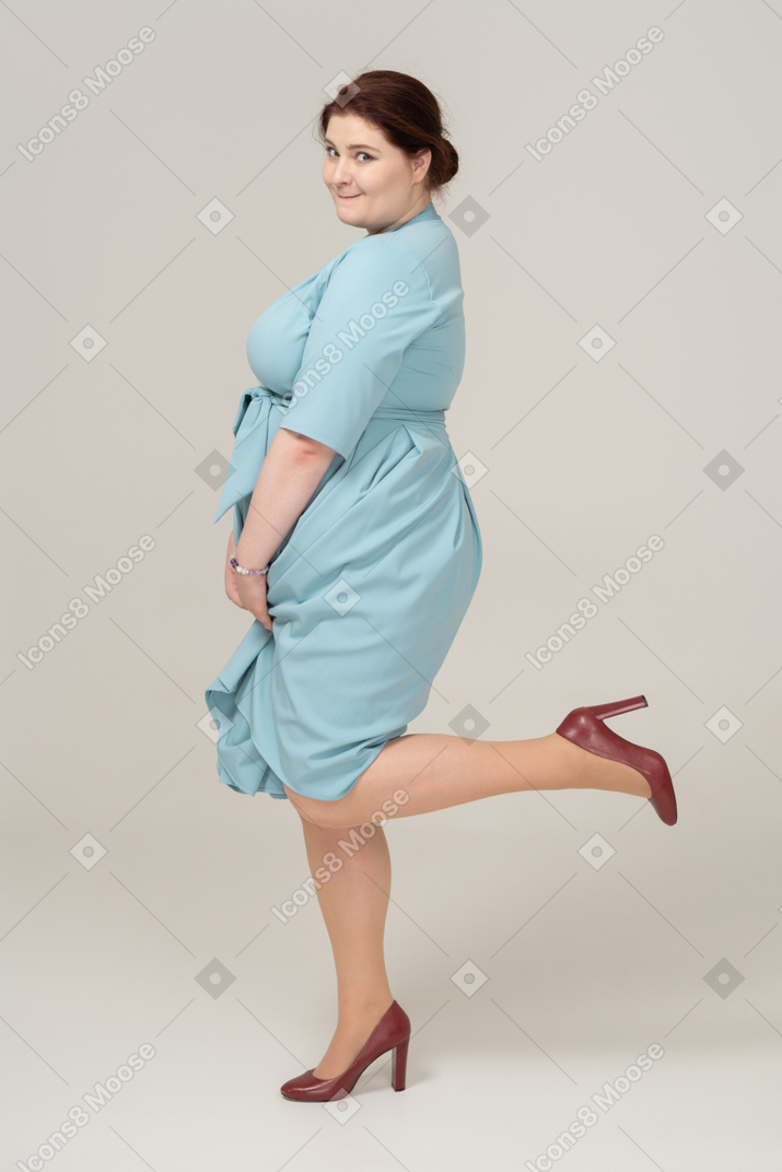 Vista lateral de uma mulher de vestido azul posando em uma perna