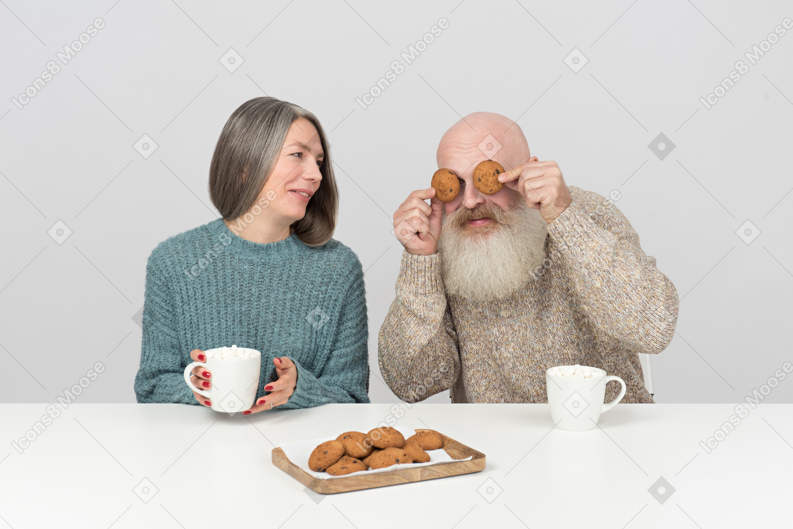 Elder man covering his eyes with cookies sitting next to his wife