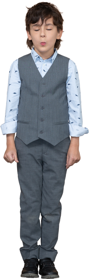 Vista frontal de un chico de cuit en traje gris de pie con los ojos cerrados