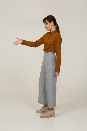 Vista laterale di un saluto giovane donna asiatica in calzoni e camicetta che tende la mano