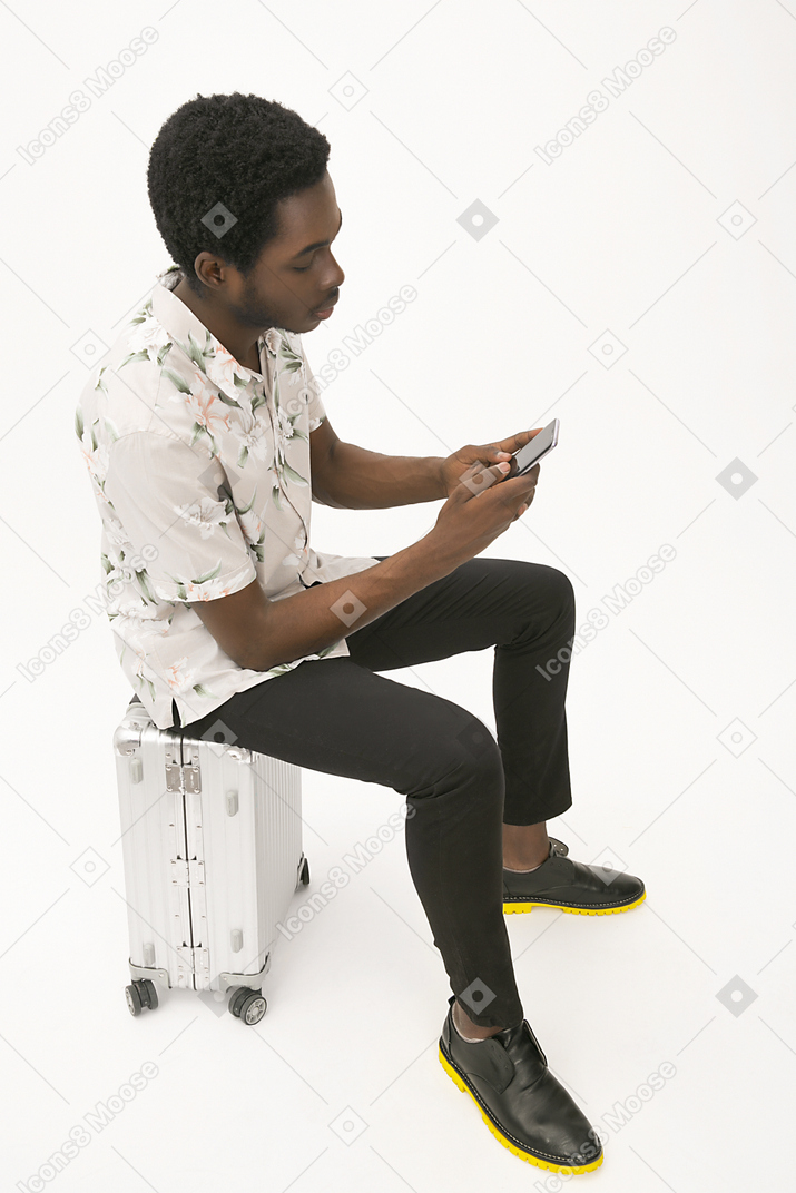Afroman sentado en el equipaje y usando su teléfono inteligente.