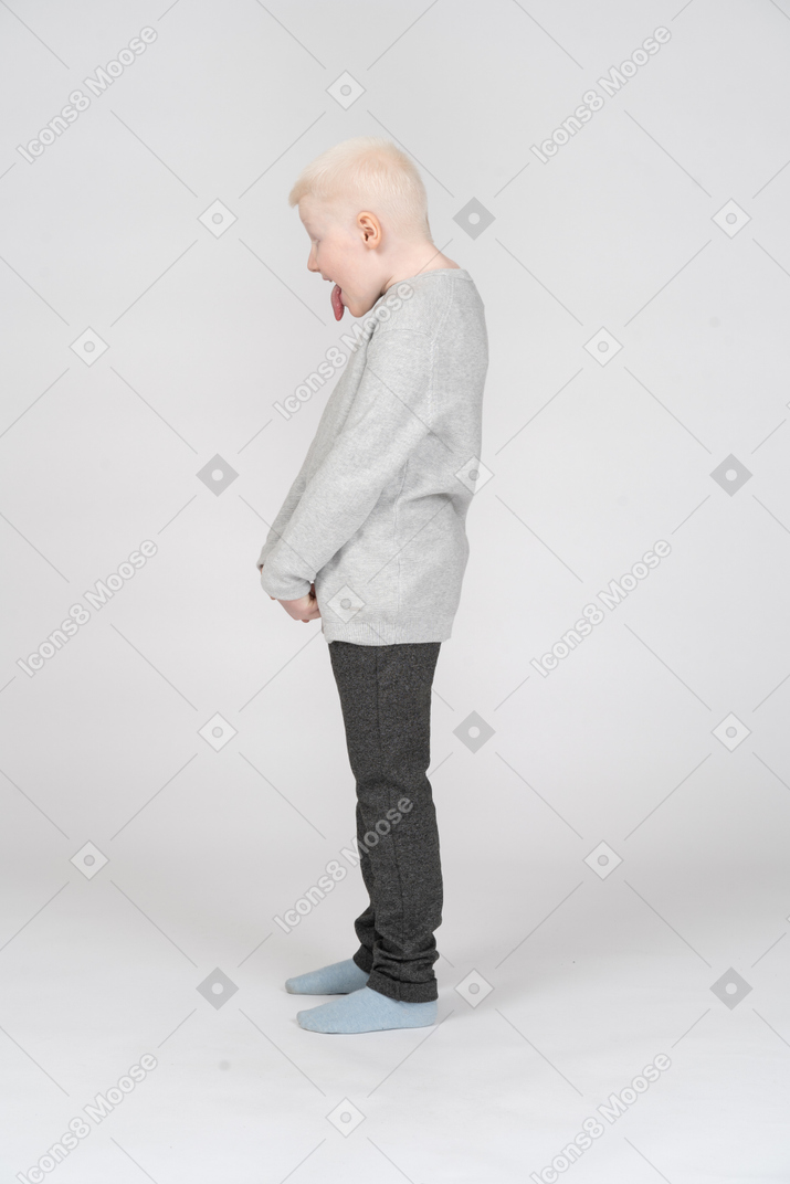 Side view of a kid boy in casual clothes showing tongue and looking down