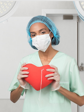 A woman wearing a surgical mask holding a heart