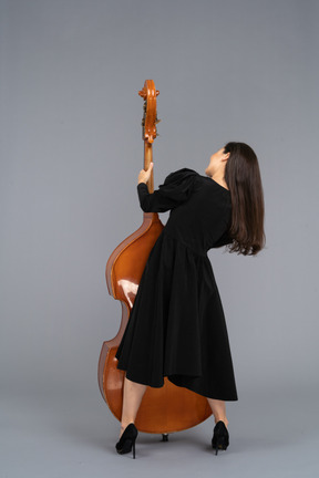 Vista posterior de un joven músico en vestido negro sosteniendo su contrabajo