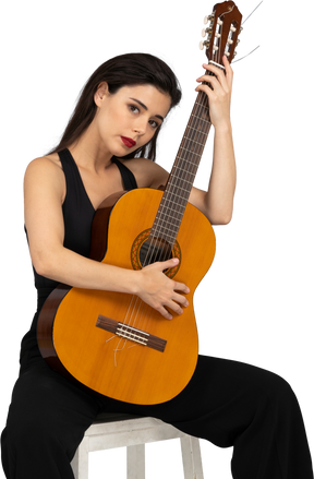 Front view of a sitting young lady in black suit embracing her guitar