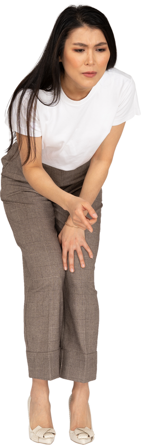 Vista frontale di una giovane donna perplessa in calzoni e maglietta chinandosi