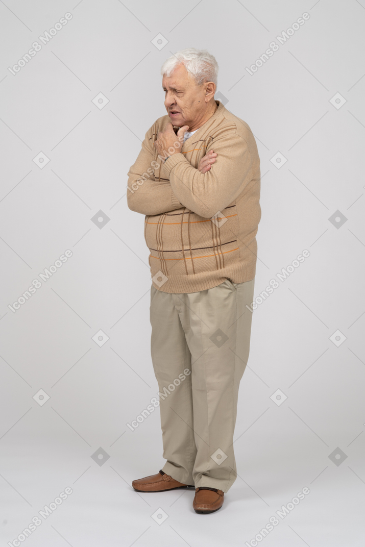 Front view of a thoughtful old man in casual clothes standing with hand on chin