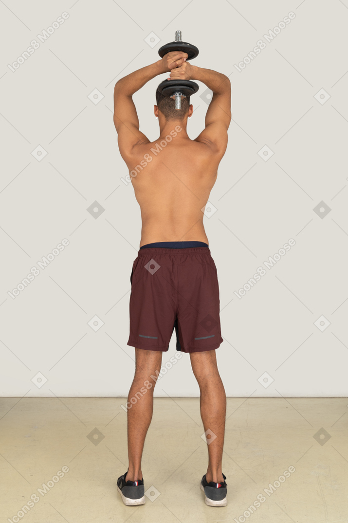 A backside view of the muscular young guy dressed in red shorts with a dumbbell in his hands