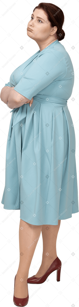 一个穿着蓝色连衣裙的女人双臂交叉站立的侧视图