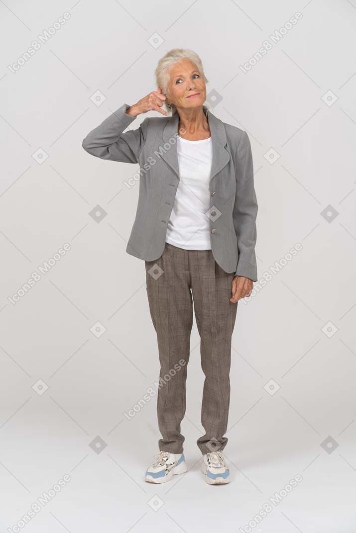 Vista frontal de una anciana en traje haciendo un gesto de llamada telefónica
