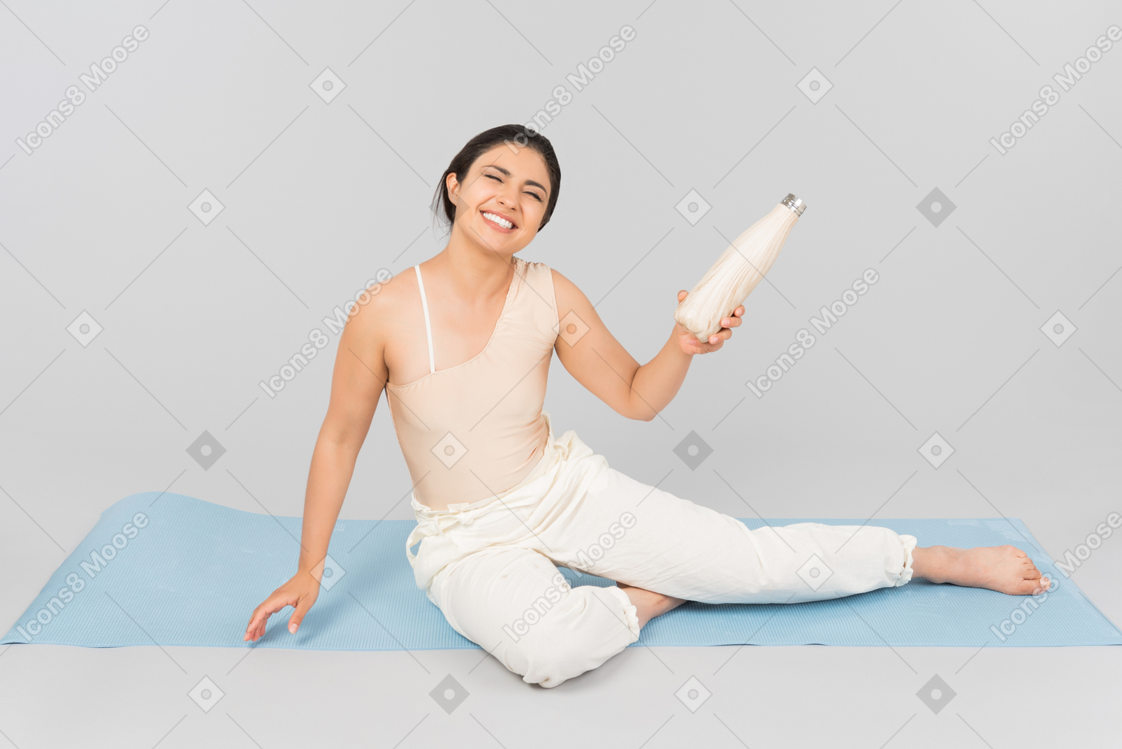 Junge indische frau, die auf yogamatte sitzt und sportflasche hält
