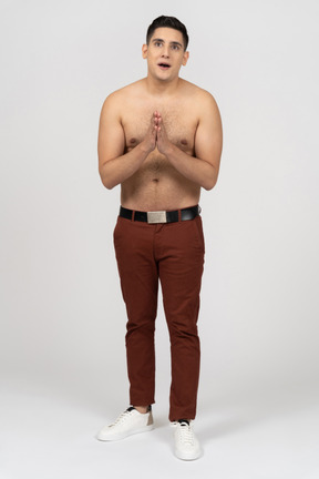 Vista frontal de um homem latino sem camisa, de mãos dadas com admiração