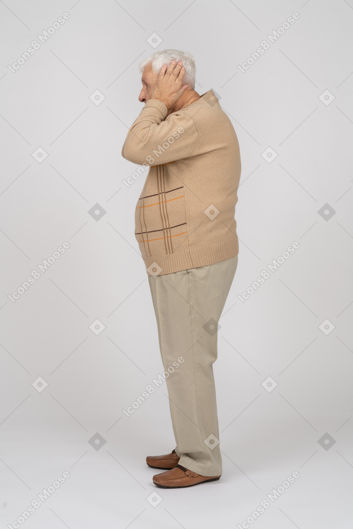 Seitenansicht eines alten mannes in freizeitkleidung, der die ohren mit den händen bedeckt