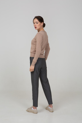 Three-quarter back view of a worried young lady in pullover and pants turning away