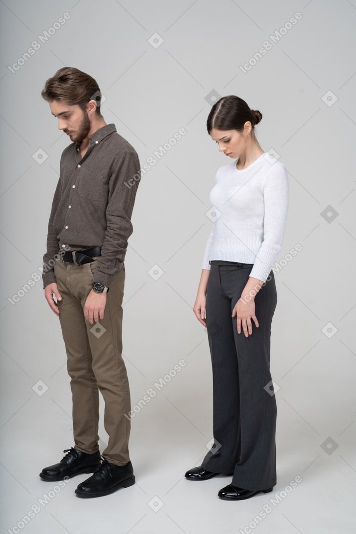 Vue de trois quarts d'un jeune couple en vêtements de bureau regardant vers le bas