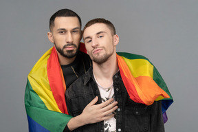 Front view of two young men half-hugging and wearing lgbt flag