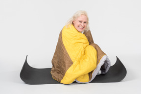 Mature woman sitting on yoga mat wrapped in blanket