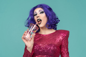 Drag queen en vestido rosa de lentejuelas bebiendo de un vaso de plástico