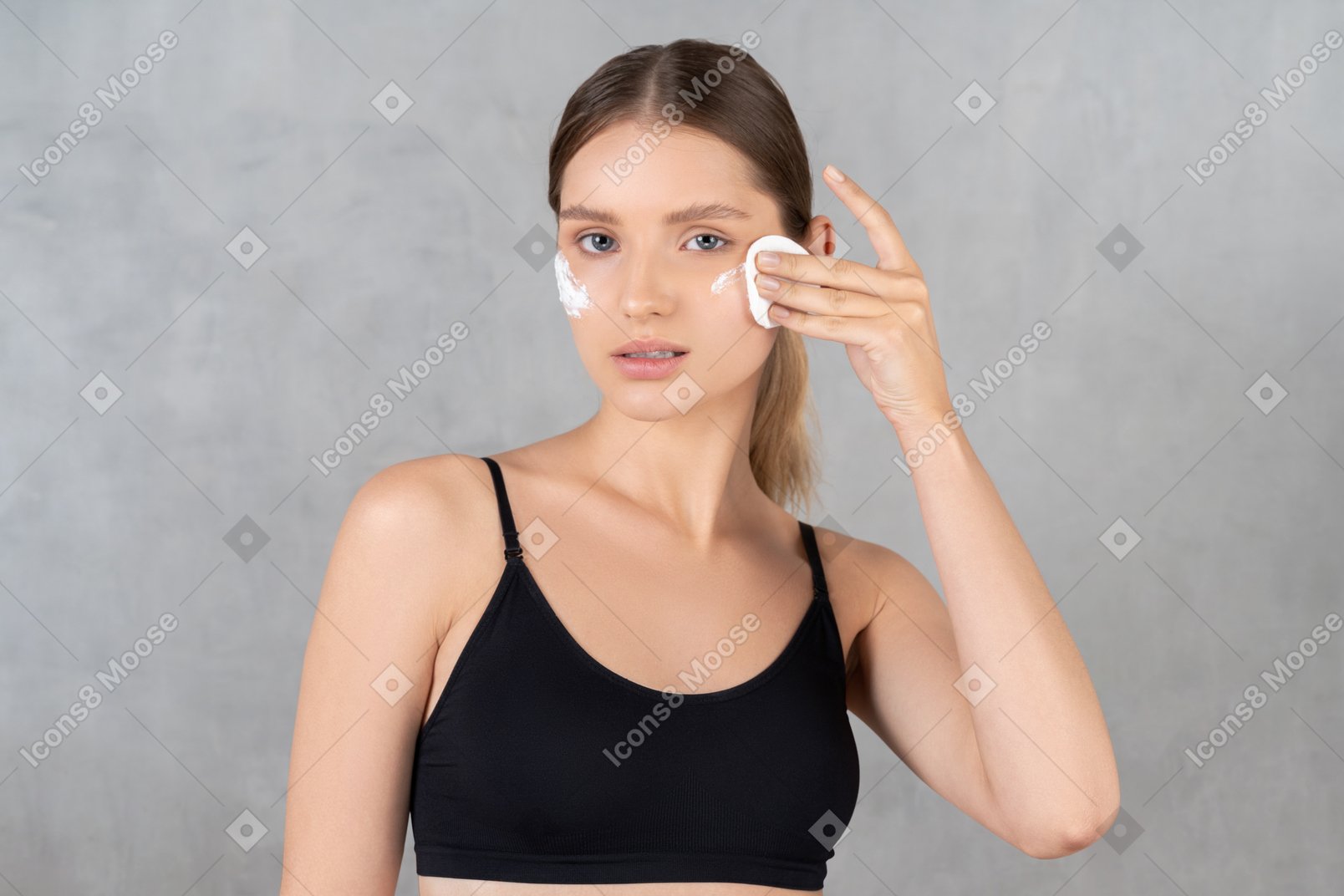 Woman removing face cream with cotton pad