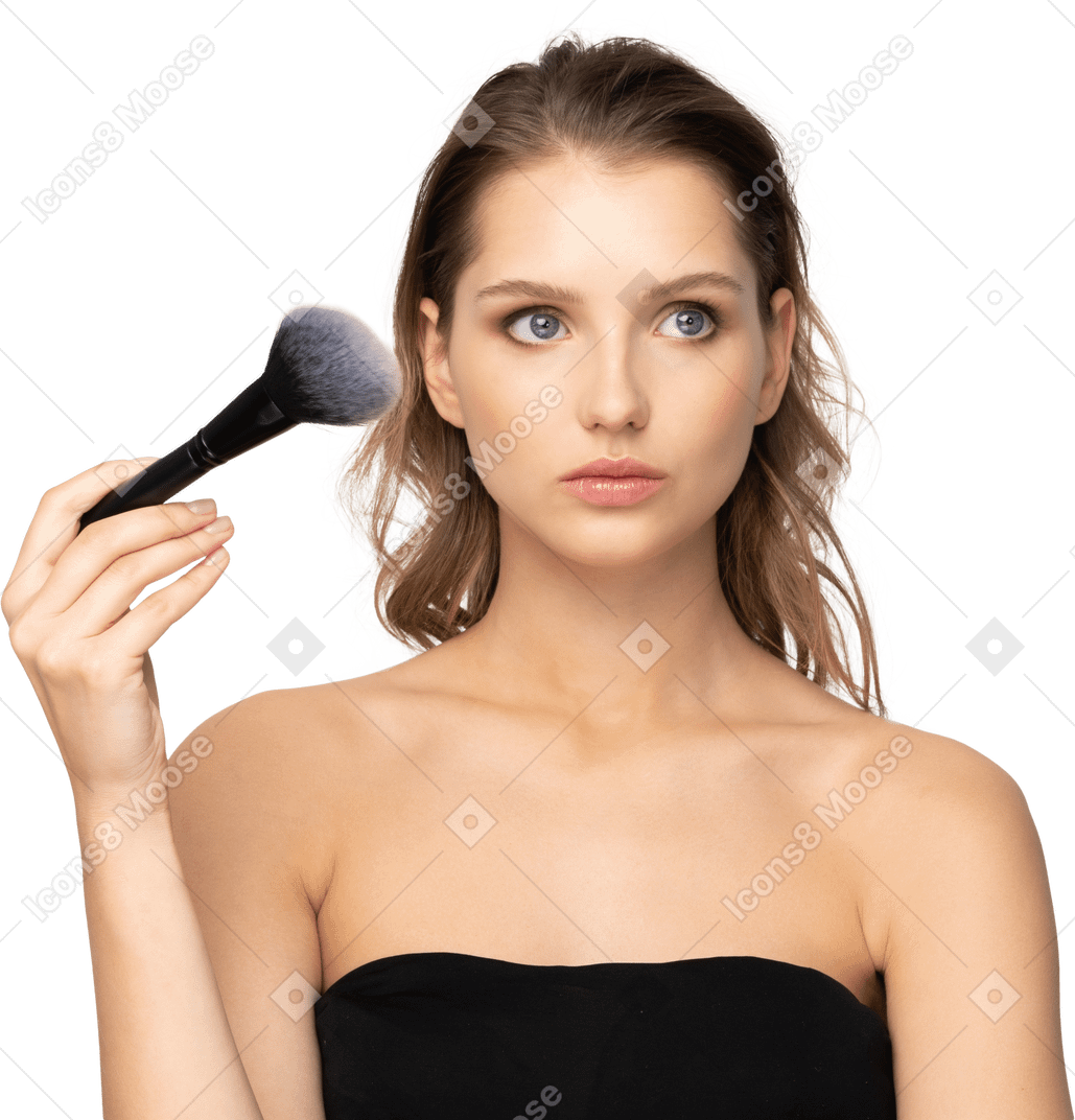 Вид спереди вдумчивой чувственной молодой женщины, держащей кисть для макияжа