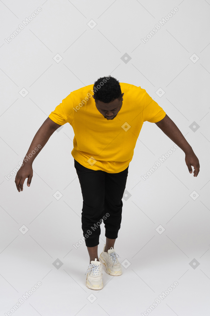 Front view of a young dark-skinned man in yellow t-shirt leaning forward & outstretching arm