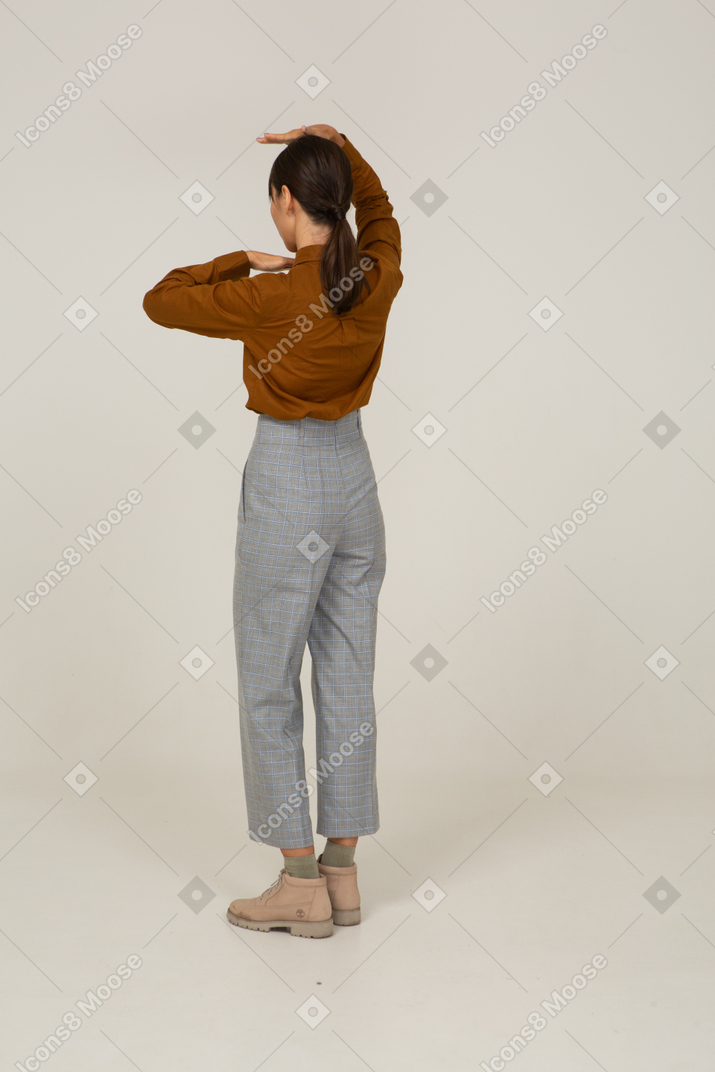 Vista de três quartos de uma jovem mulher asiática de calça e blusa mostrando o tamanho da cabeça