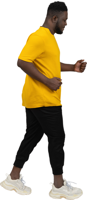 一个穿着黄色 t 恤的黑皮肤青年行走的侧视图
